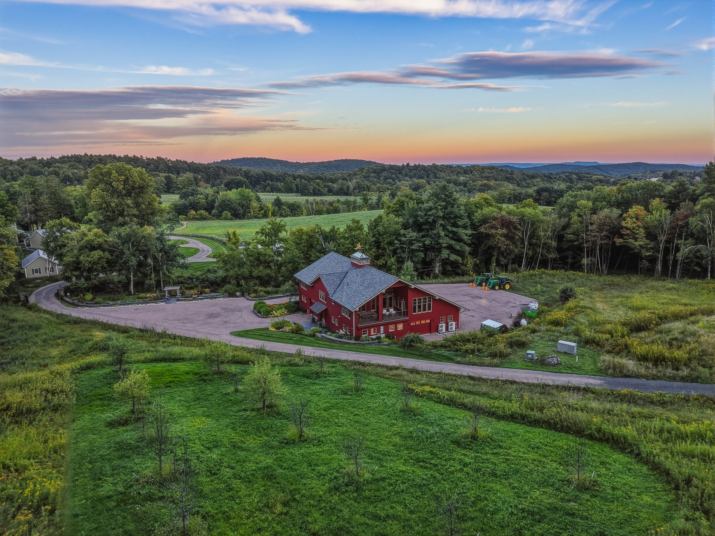 Aerial view of the estate at dusk: the residence, the red barn and open meadows surrounded by woodland